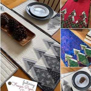 May include: A quilted table runner and placemat set with a Scandinavian design. The table runner is 14 inches by 37 inches, and the placemats are 12.5 inches by 18.5 inches. The design features geometric shapes in shades of gray and white, with a tag that says "Freezer Paper Piecing!"