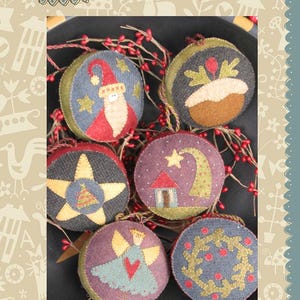 May include: Six round fabric ornaments featuring embroidered Christmas motifs including Santa, a pudding, a star with a tree, a house with a star, an angel, and a wreath. The ornaments are decorated with red berries and have the text Hatched and Patched.