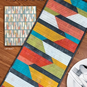 May include: A colorful geometric table runner with a pattern of black, white, yellow, red, green, and blue. The runner is on a wooden surface with a white plate and silverware. The text "MONORAIL" is at the top of the image and "ATK-211" is at the bottom.