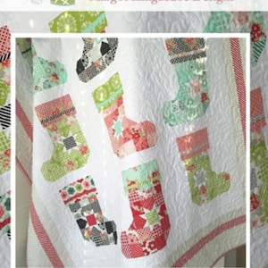 May include: A white quilt featuring appliqued Christmas stockings in various patterns and colors, including red, green, and black. The quilt has a quilted texture and the text "Ready for Santa" is visible.