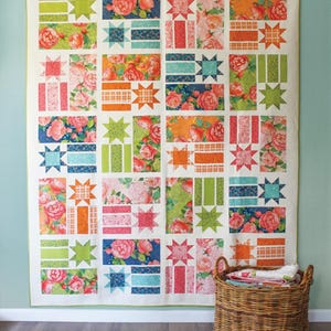 May include: A quilt pattern called "Constance" by Robin Pickens Quilt Patterns. The quilt features a patchwork design with floral fabric, stars, and stripes in shades of pink, orange, green, blue, and white. The quilt is available in three sizes: lap, twin, and queen.