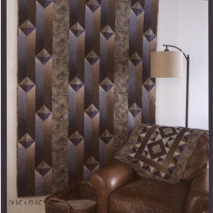 May include: A quilt with a geometric design in shades of brown, gray, and blue, hanging on a wall. The quilt measures 51 x 78 inches. The image also shows a leather armchair, a pillow, and a wicker basket. The text "Gentlemen's Agreement" is at the top.