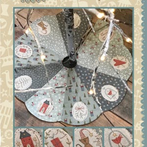 May include: A circular Christmas tree skirt with a scalloped edge, featuring a patchwork design in shades of gray and blue. The skirt has embroidered motifs of houses, gifts, and animals. The text "Hatched and Patched" and "The Giving Tree Skirt" are visible.