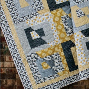 May include: A quilting pattern called "Tabitha" by Swirly Girls. The pattern is fat quarter friendly and features a geometric design in yellow, gray, and black fabrics.