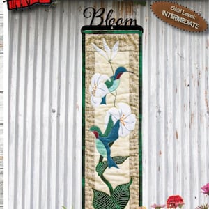 May include: A vertical fabric wall hanging featuring hummingbirds and white flowers, with the word "Bloom" at the top. The dimensions are 6 inches by 22 inches. The skill level is intermediate.