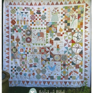May include: A colorful patchwork quilt with the text "SUNSHINE & LOLLIPOPS" at the top. The quilt features various patterns, including squares, circles, and triangles, with images of an elephant, birds, and teacups. The quilt is made of various fabrics in shades of red, blue, green, and yellow.