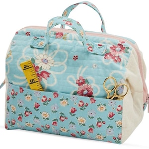 May include: A light blue quilted sewing bag with a floral print and a white zipper. The bag has a top handle and a front pocket with a yellow measuring tape and gold scissors.