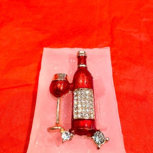 May include: A pink silicone mold for making a wine bottle and glass. The mold is filled with a red wine bottle and glass with rhinestones.