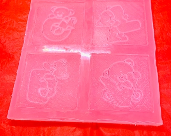 May include: A pink silicone mold with four sections, each featuring a raised design of a teddy bear. The mold is designed for making soap or other crafts.