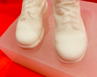 Könnte beinhalten: Eine weiße Silikonform zum Herstellen von zwei Paaren Mini-Stiefeletten. Die Form steht auf einer roten Oberfläche.