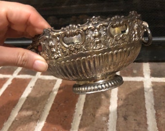 May include: A silver bowl with an ornate design and a fluted base. The bowl has a scalloped edge and two handles.