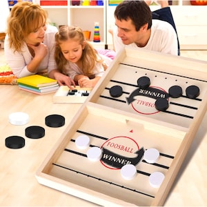 Pode incluir: Um jogo de tabuleiro de madeira com duas áreas de jogo. Uma área é etiquetada como "Foosball Winner" e a outra como "Osbball Winner". O jogo inclui peças de jogo pretas e brancas.