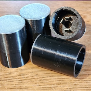 May include: Four black plastic cylindrical objects, three with smooth tops and one with a center hole and three small metal prongs. The objects appear to be 3D printed.