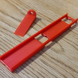 May include: A red plastic ramp with a smaller red plastic piece that fits into the ramp. The ramp has a slot in the middle.