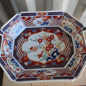 May include: Octagonal serving tray with two handles, featuring a white background with a floral design in shades of red, blue, and green. The tray has a gold trim and a red and blue geometric pattern around the edge.
