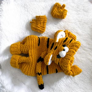May include: A handmade, mustard yellow tiger costume with black stripes, including a matching hood and paw covers. The costume is made of soft, textured yarn and is designed for a baby or toddler.