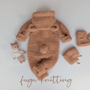 May include: A light brown, knitted baby outfit set, including a jumpsuit with bear ears, booties, and a small teddy bear toy. The jumpsuit has long sleeves and a turtleneck collar. The booties have a tie closure. The teddy bear is wearing a white shirt.