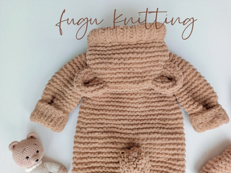 May include: A light brown, knitted baby jumpsuit with a high collar and long sleeves. The jumpsuit has a textured, plush appearance and features a small pocket on the front. The words "fugu knitting" are written in a cursive font.