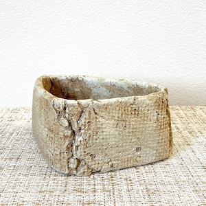 May include: A small, rectangular, light brown planter with a rough, textured surface. The planter is made of ceramic and has a slightly irregular shape.