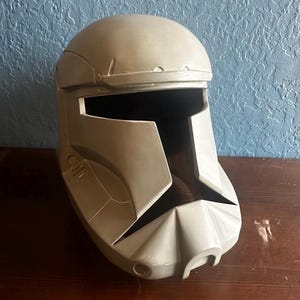 May include: A gray plastic helmet with a visor and a textured surface. The helmet has a design that resembles a futuristic soldier's helmet.