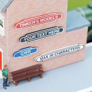 May include: A miniature brick building with a red, black, blue, and white sign that reads "Tinker's Models", "Your Text Here", "GWR", and "Max 20 Characters".
