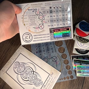 May include: A set of colorful stickers featuring a variety of designs, including circles, squares, and text. The stickers are on a wooden surface. The text on the stickers includes "Loving & Wholesome", "Sirales Essentials Kit", and "$18.00".