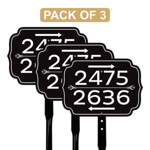 May include: A pack of three black address signs with white numbers and arrows. The signs have an ornate border and are mounted on black posts. The text "PACK OF 3" is in a gold rectangle at the top.
