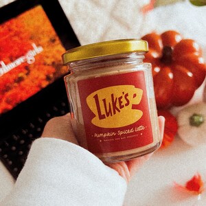 May include: A glass jar with a gold lid filled with a brown substance. The jar has a red and yellow label that says "Luke's" and "Pumpkin Spiced Latte".