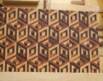Könnte beinhalten: Rechteckiges Holzschneidebrett mit einem geometrischen Muster aus ineinandergreifenden Würfeln. Das Design verwendet verschiedene Brauntöne, wodurch ein dreidimensionaler Effekt entsteht. Das Brett ist wahrscheinlich für den Küchengebrauch.