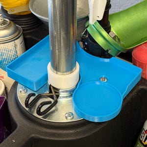 May include: A close-up shot of a blue plastic tray with a circular indentation and a rectangular section. A silver metal pole is in the center, with various tools and containers in the background.