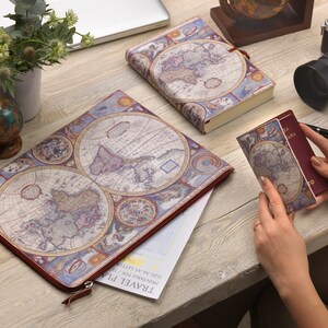 May include: A red leather travel journal with a vintage world map design. The journal is open to reveal a blank page with the words "TRAVEL PLAN" printed at the top. The journal is surrounded by other travel-themed items, including a globe, a camera, and a passport.