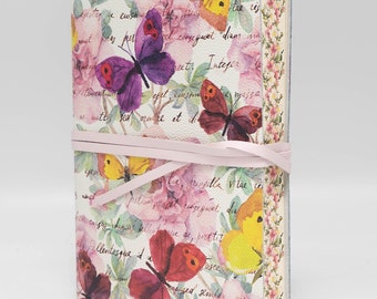 Puede incluir: Un diario rosa y blanco con un diseño floral con mariposas y texto escrito a mano. El diario está atado con una cinta rosa.