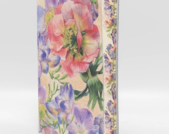Puede incluir: Una caja rectangular con un diseño floral. La parte delantera presenta una gran flor rosa y amarilla rodeada de flores moradas y azules y hojas verdes. El lateral de la caja tiene un borde de flores moradas y rosas más pequeñas.