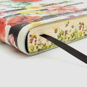 May include: A floral journal with a black ribbon bookmark. The cover features a pattern of red poppies, yellow flowers, and black and white stripes. The inside edge has a bee and flower illustration.