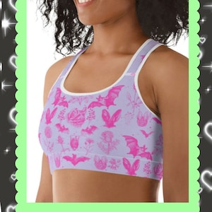 Puede incluir: Un conjunto de sujetador deportivo y leggings rosa y blanco con un estampado gráfico de murciélagos, flores y corazones. El texto "CHECK OUT MOODYsunday ON ETSY TO COMPLETE THE LOOK!" está en la parte inferior de la imagen.