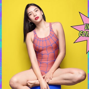 Może przedstawiać: Kobieta w czerwono-niebieskim kostiumie kąpielowym z wzorem pajęczyny. Kostium kąpielowy ma styl racerback. Kobieta siedzi na niebieskim sześcianie na ż&oacute;łtym tle. Tekst "Vintage Colouring!" znajduje się w r&oacute;żowej chmurce. Tekst "Check out Moody Sunday on Etsy" znajduje się na dole obrazu.