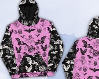 Pode incluir: Moletom rosa com capuz com estampa de morcegos e flores em preto e branco. O moletom tem um capuz preto e um grande bolso na frente. A parte de trás do moletom tem a mesma estampa que a frente. O texto "CHECK OUT MOODY SUNDAY ON ETSY" está impresso na parte inferior da imagem.