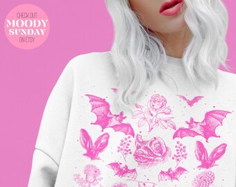 May include: White sweatshirt with a pink print of bats, flowers, and other botanical illustrations. The text "CHECK OUT MOODY SUNDAY ON ETSY" is printed in pink at the top of the sweatshirt.