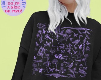 Op de afbeelding: Zwart sweatshirt met een gedetailleerde paarse afbeelding met verschillende dierenskeletten, vlinders, bloemen en insecten. De tekst linksboven luidt "FOR AN OVERSIZED FIT GO UP A SIZE OR TWO!"