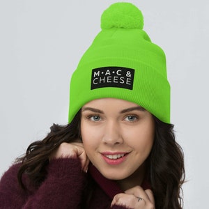 May include: A bright green beanie with a black pom pom on top. The beanie has a black patch with the text "M.A.C & CHEESE" in white.