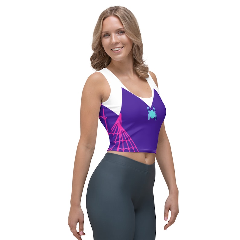 Puede incluir: Un top corto morado y blanco con un dise&ntilde;o de telara&ntilde;a rosa y un gr&aacute;fico de ara&ntilde;a azul. El top tiene un racerback blanco y un frente morado con un dise&ntilde;o de telara&ntilde;a rosa. La ara&ntilde;a es azul con un contorno blanco.