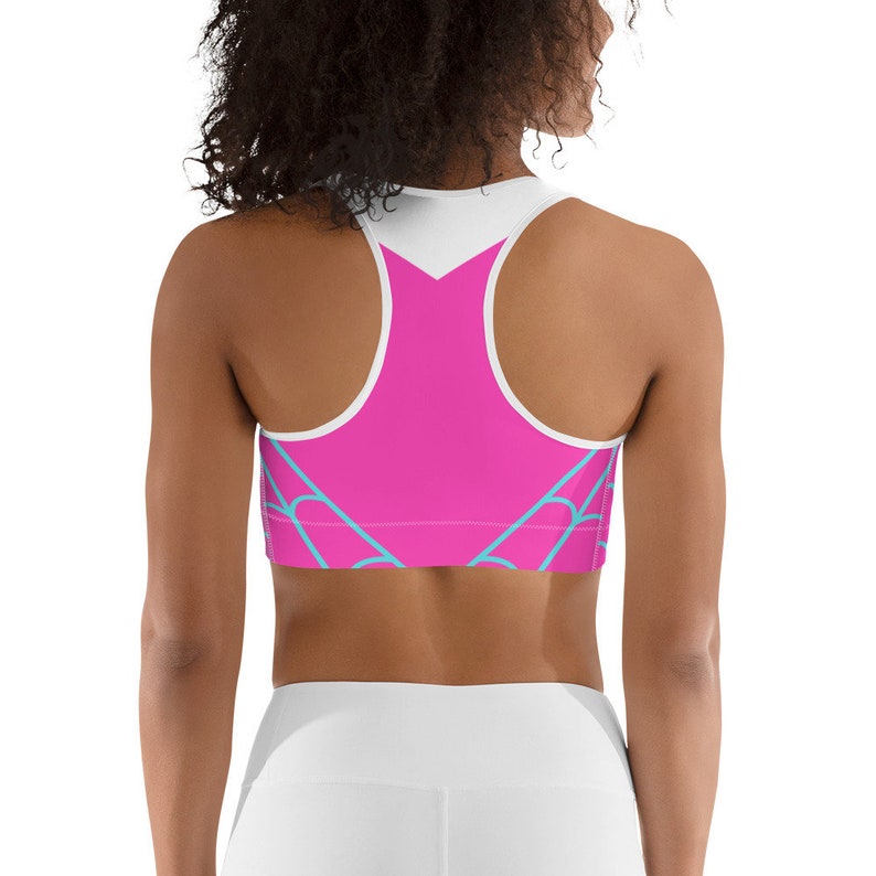 May include: A pink sports bra with a white back and blue geometric design. The bra has a racerback style.