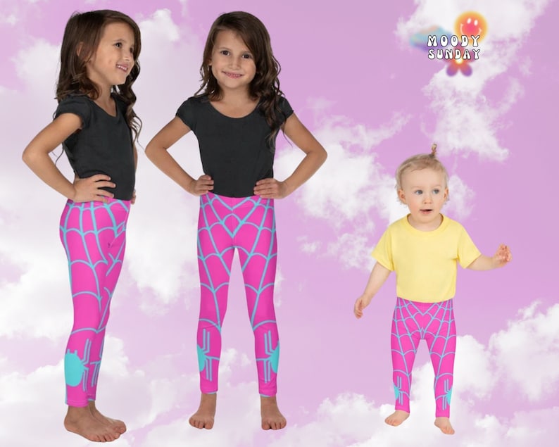 Op de afbeelding: Drie kinderen dragen roze en blauwe leggings met spinnenweb-patroon. De leggings hebben een spin-afbeelding aan de onderkant van elk been. De kinderen staan voor een roze en witte achtergrond.