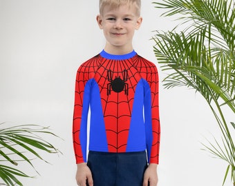 May include: A child wearing a blue and red long-sleeved shirt with a black spider web design and a black spider in the center.