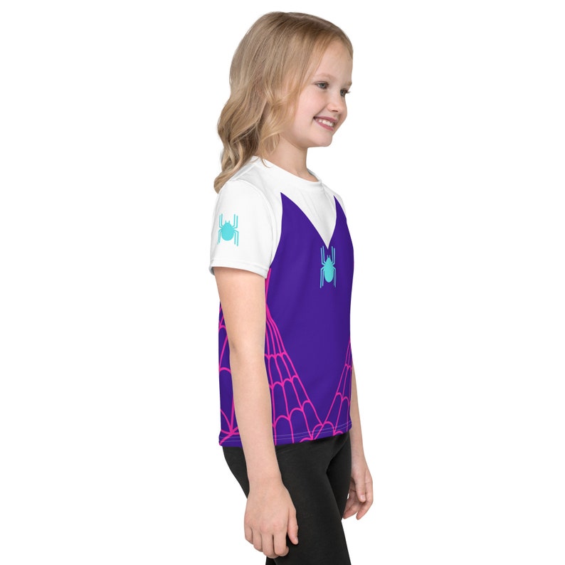May include: A white and purple t-shirt with a spiderweb design and a blue spider graphic. The shirt has short sleeves and a crew neck.