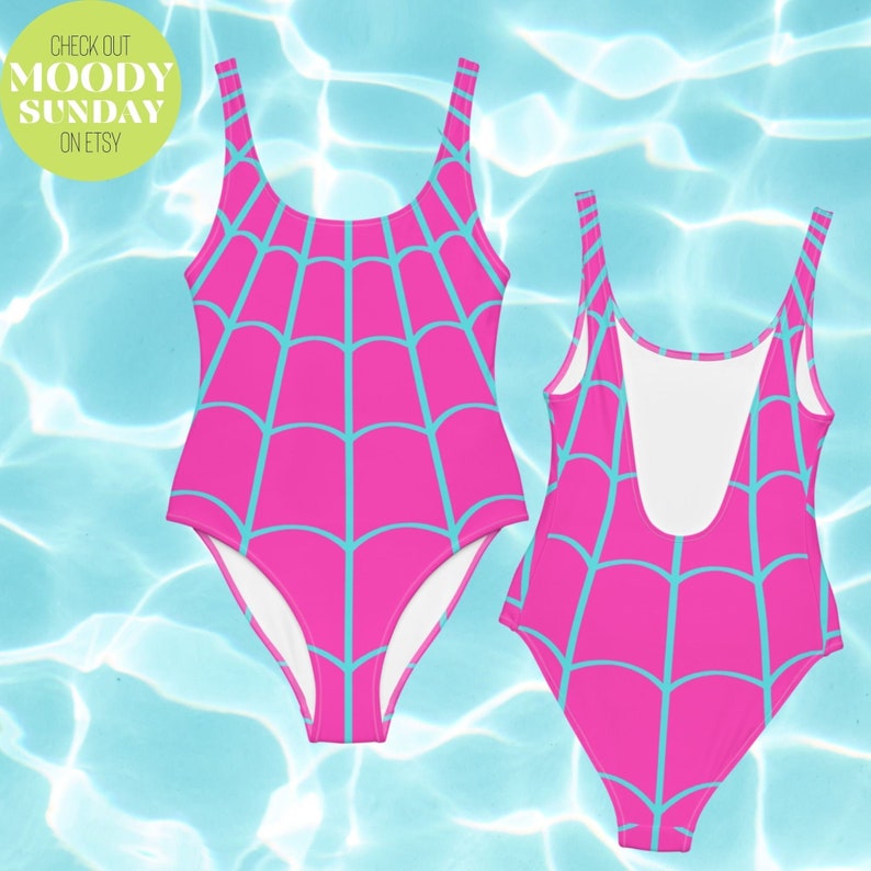 May include: A one-piece swimsuit featuring a bright pink base with a light blue spiderweb pattern. The garment has a scoop neckline and a low-cut back design. The text "CHECK OUT MOODY SUNDAY ON ETSY" is printed in a circular green badge in the corner.