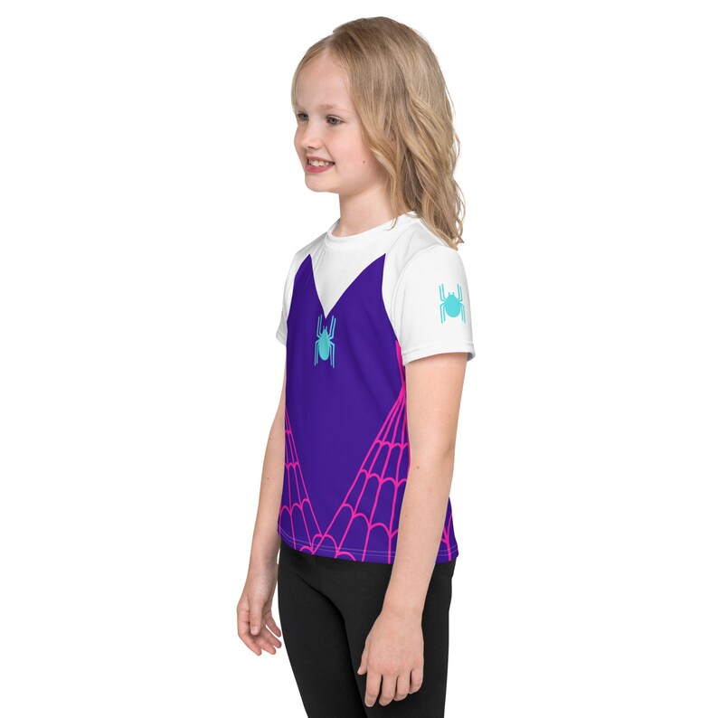 May include: A white t-shirt with a purple and pink spiderweb design. The shirt has a blue spider graphic on the front and a smaller blue spider graphic on the right sleeve.