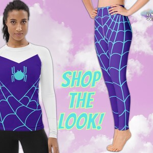 Op de afbeelding: Een wit shirt met lange mouwen met een paars en blauw spinnenwebontwerp en een blauwe spin-afbeelding. Het shirt wordt gecombineerd met paarse leggings met een paars en blauw spinnenwebontwerp. De tekst "SHOP THE LOOK!" staat in de afbeelding.