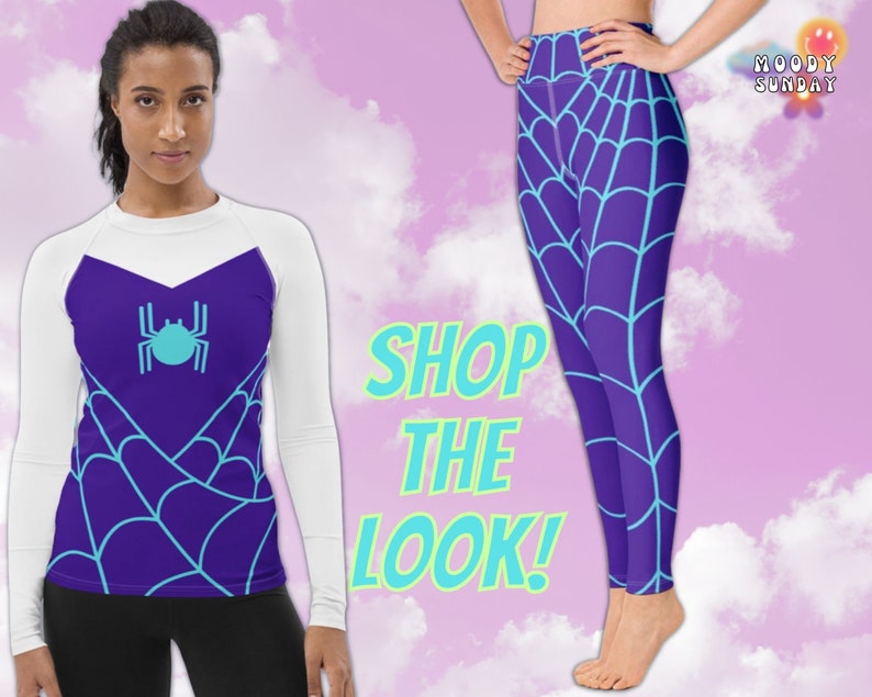 Op de afbeelding: Een wit shirt met lange mouwen met een paars en blauw spinnenwebontwerp en een blauwe spin-afbeelding. Het shirt wordt gecombineerd met paarse leggings met een paars en blauw spinnenwebontwerp. De tekst "SHOP THE LOOK!" staat in de afbeelding.