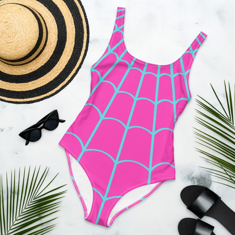 May include: A one-piece swimsuit featuring a vibrant hot pink base colour with a repeating light blue spider web pattern across the entire garment. The swimsuit has a scoop neckline and wide shoulder straps, providing a full-coverage design.